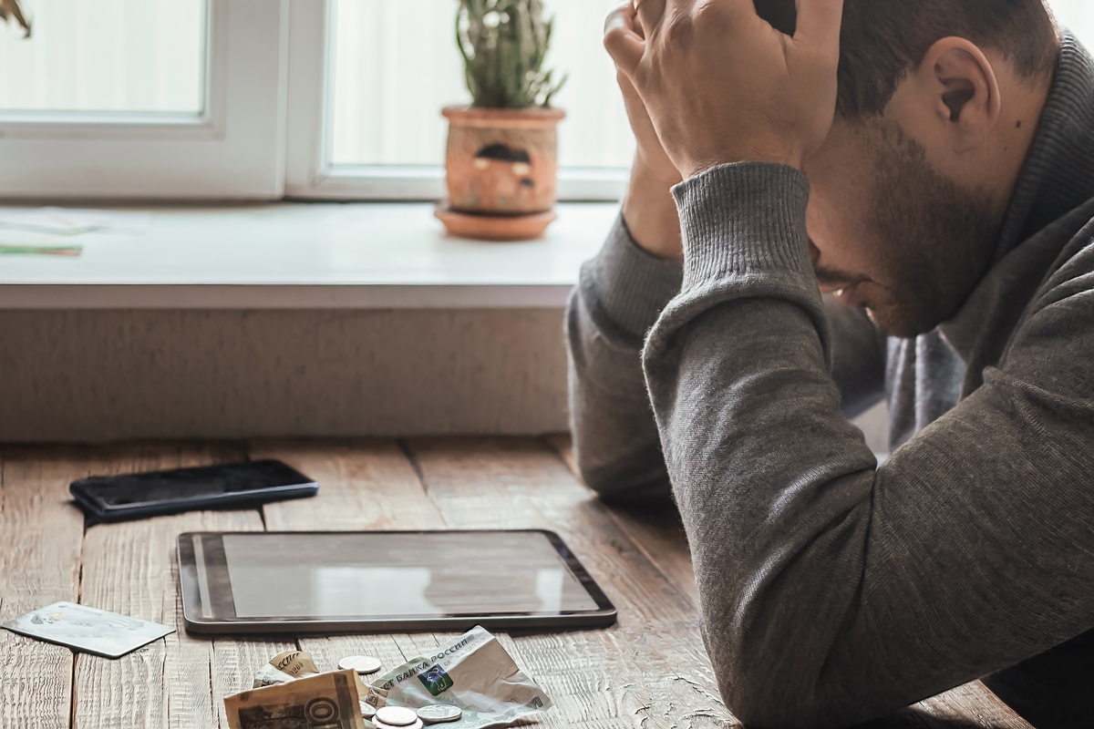 Man sitting holding his head on desk with money and tablet before him iFama explains how you can start a business with no money